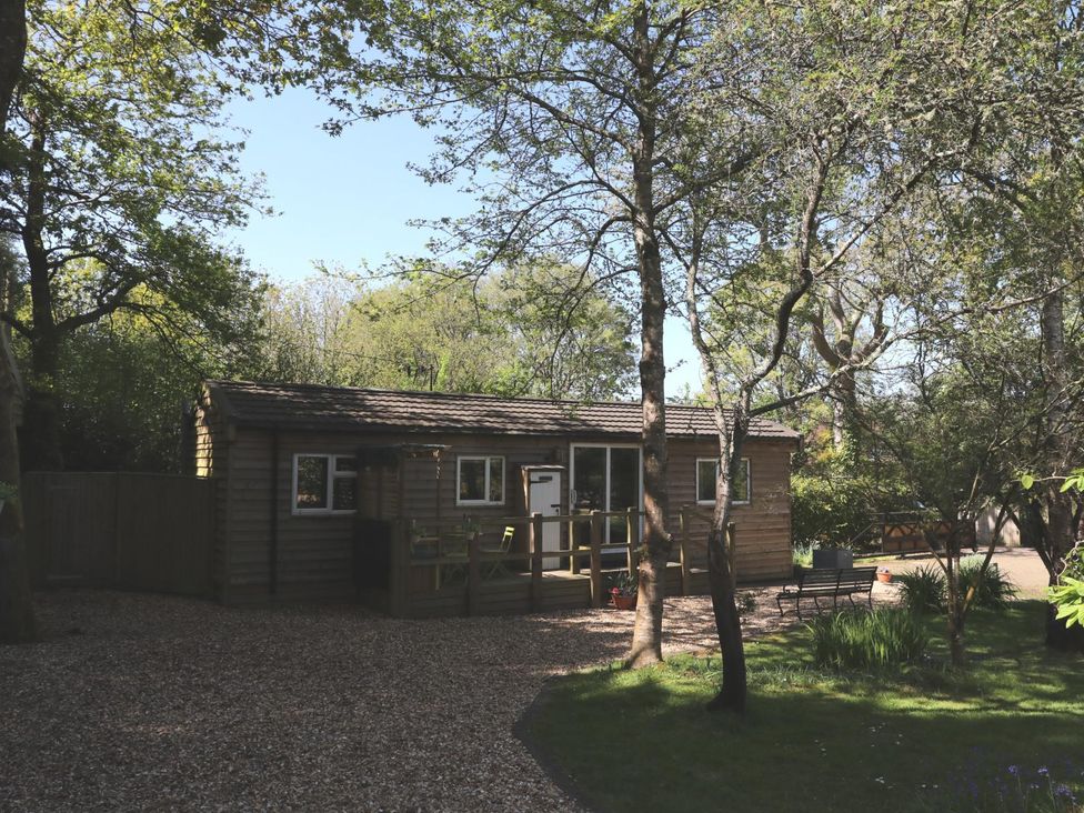 A wooden cabin with a deck surrounded by trees at Orchard Lodge Bolney