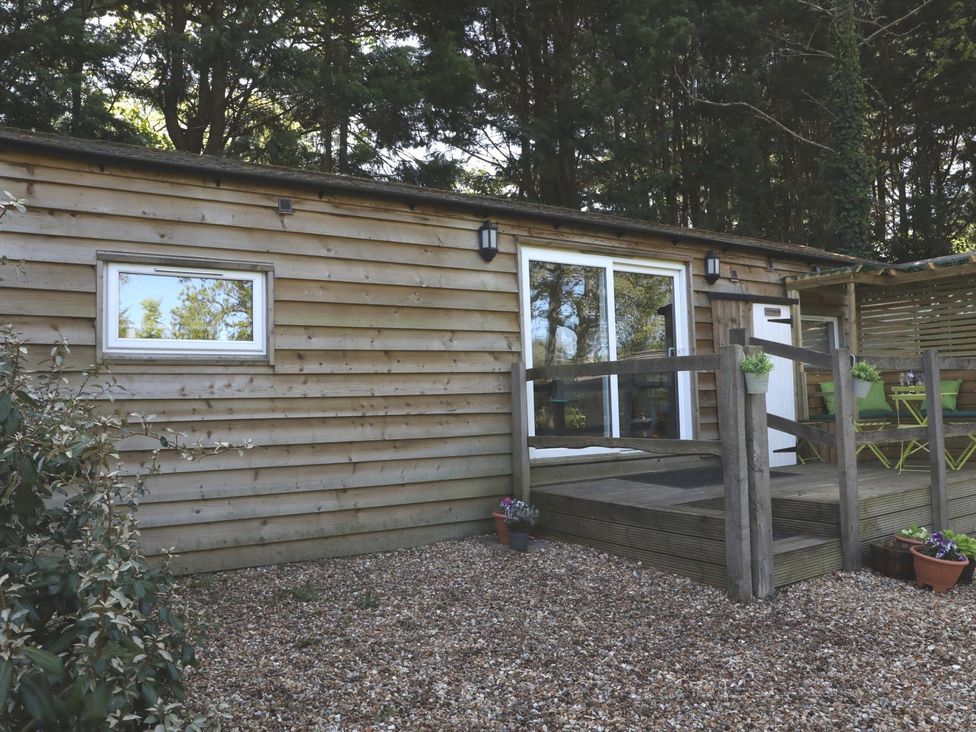 A wooden cabin with a deck and potted plants at Harvest Lodge in Wineham near Bolney