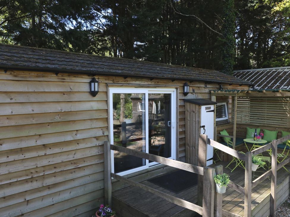 An outdoor area of a wooden cabin with a deck and seating at Harvest Lodge in Wineham near Bolney