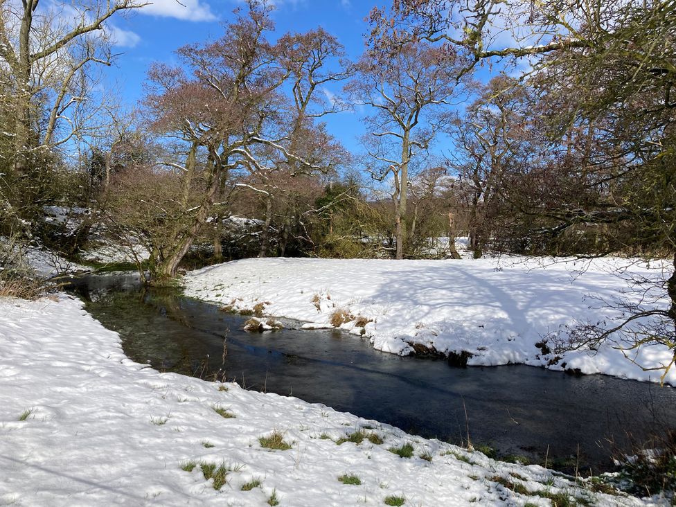 A winter scene with snow and a stream surrounded by trees at Beechwood Cottage in Easby near Great Ayton