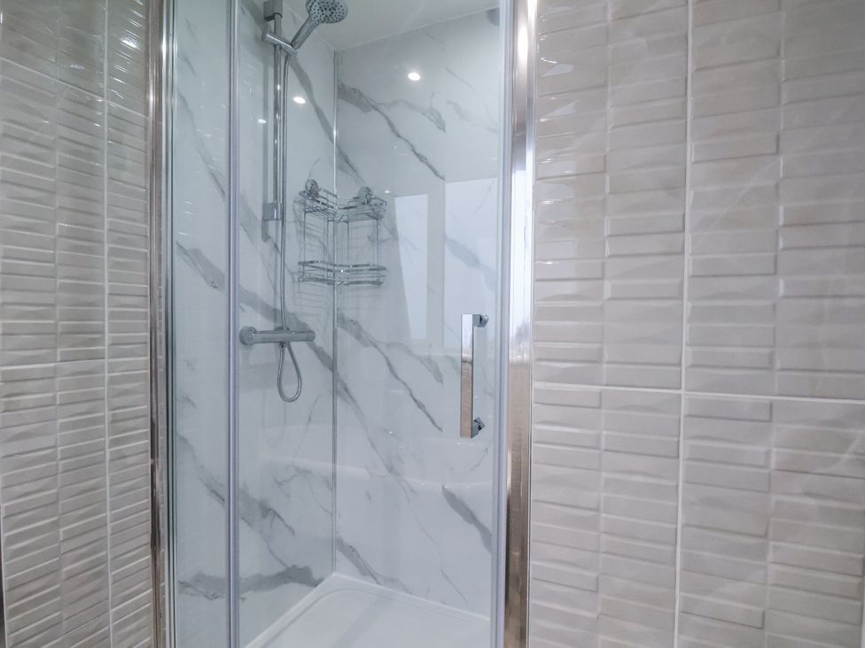 A shower with glass enclosure and tiled walls at Beachcrest in Whitby