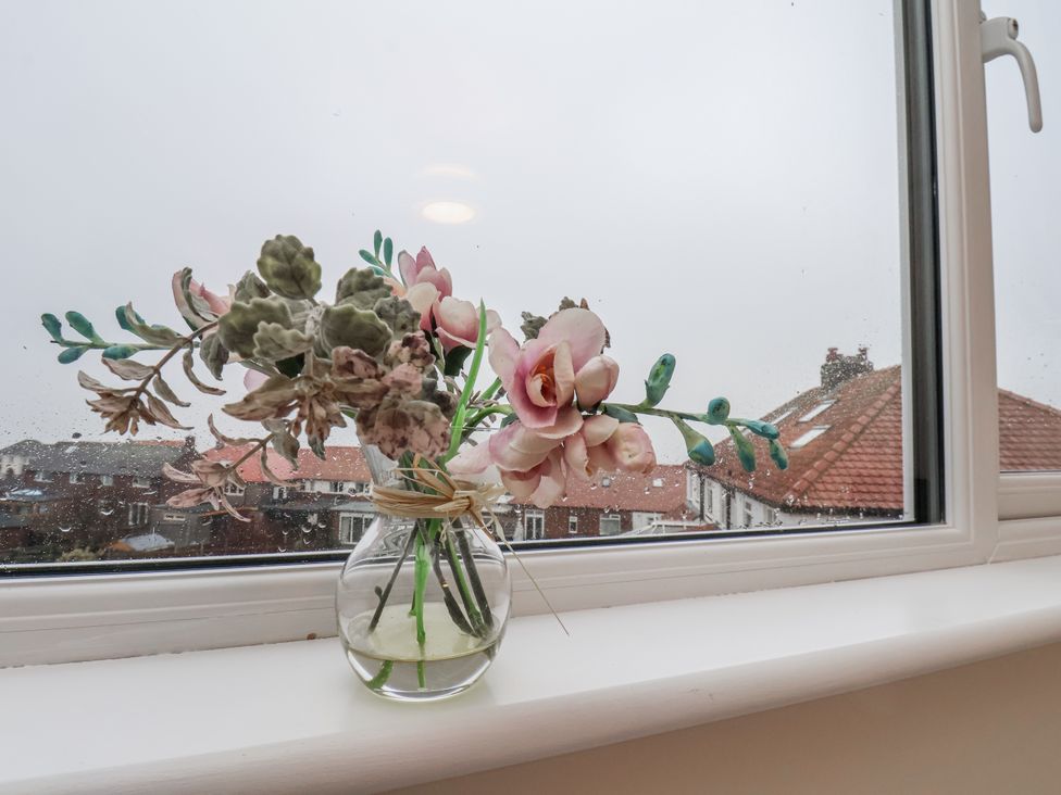 A window with a vase of flowers and rooftops visible outside at Beachcrest Whitby
