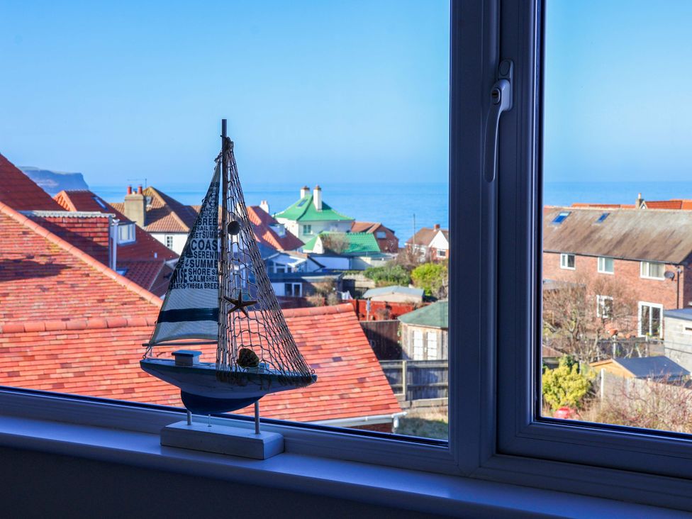 A sailboat on a windowsill with a view of the sea and houses at Beachcrest in Whitby