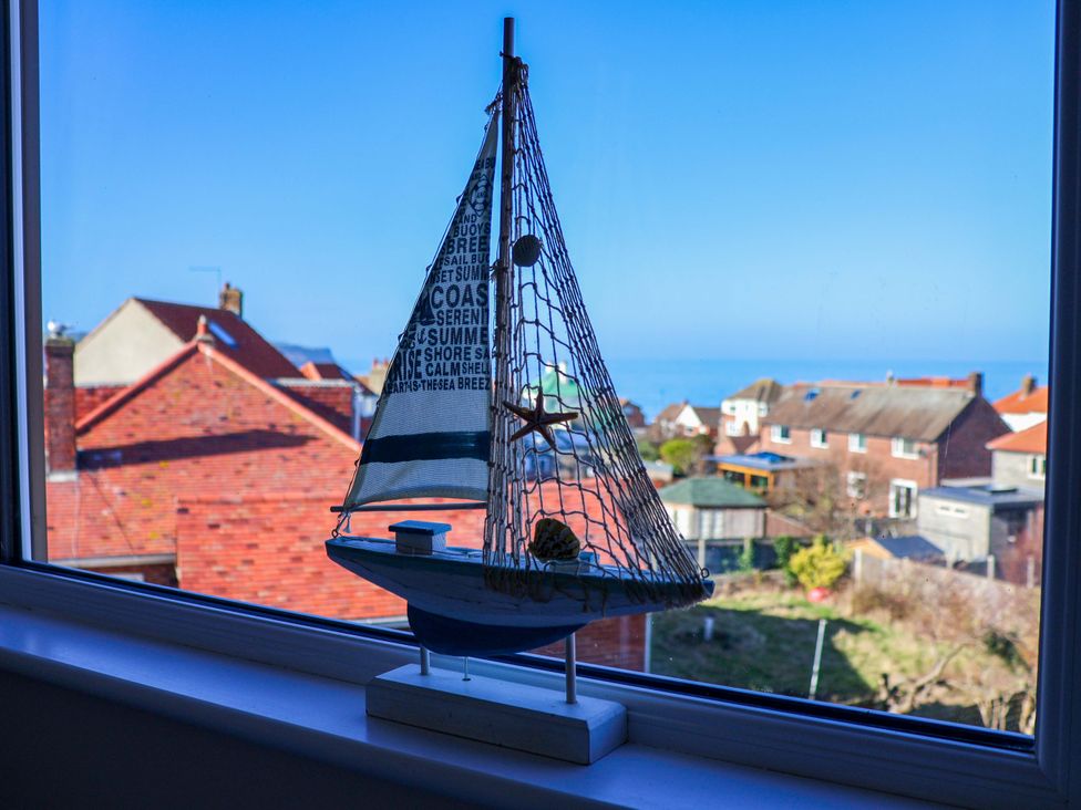 A sailboat decoration on a windowsill with a view of houses and the ocean at Beachcrest in Whitby