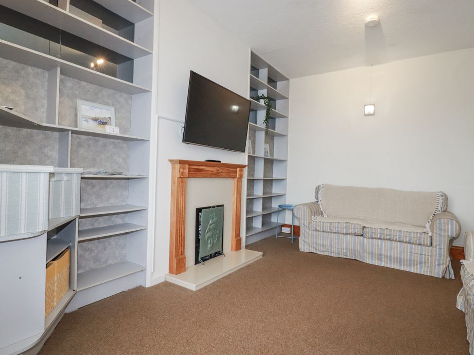 A living room with a television, shelf, sofa, and fireplace at The Three Tees in Newquay