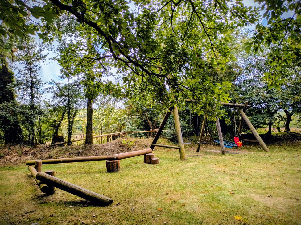 An outdoor playground with a swing set and wooden logs at Pond Meadow in Warbstow