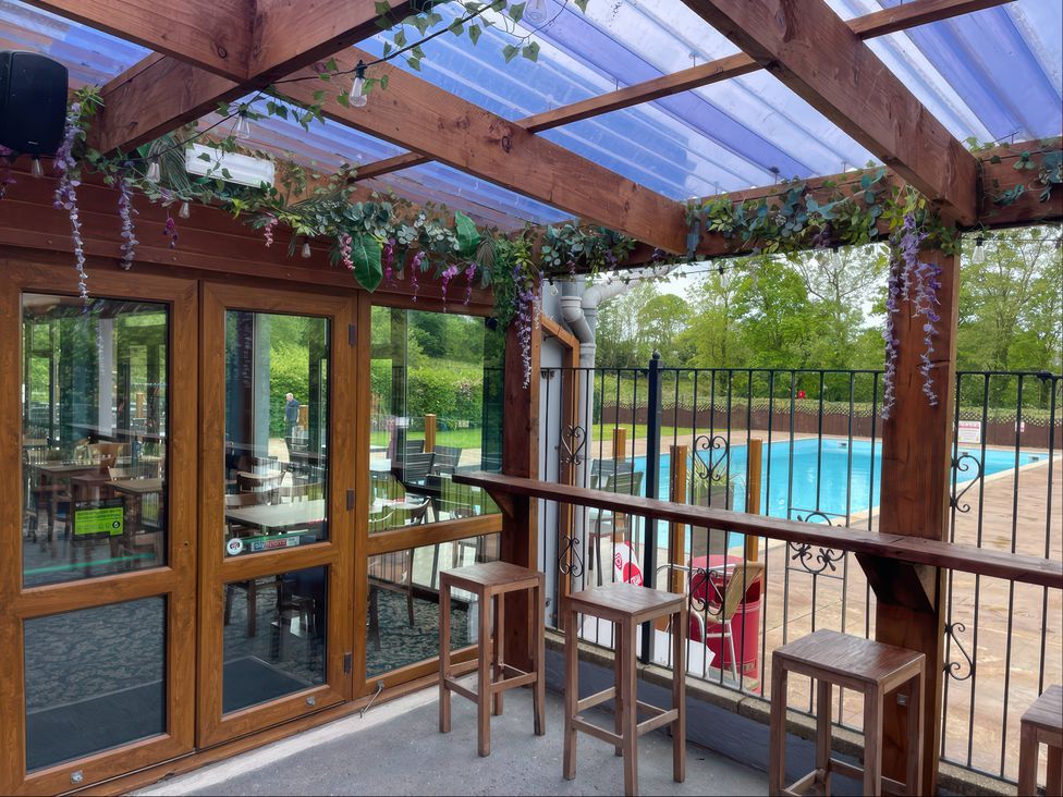 An outdoor seating area with bar stools and a pool at Eirlys in Caeathro near Caernarfon