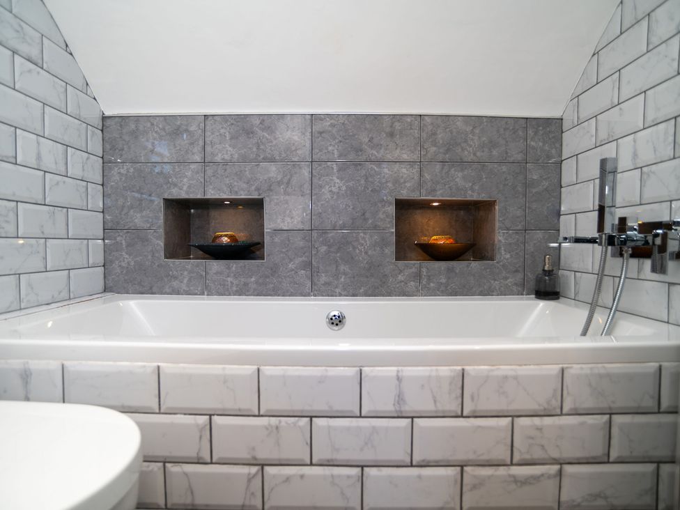 A bathroom with a bathtub and wall tiles at Garden View Apartment in Kingsbridge