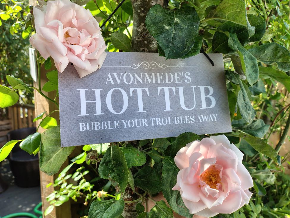 A sign indicating Avonmede's hot tub in a garden with roses in Tewkesbury