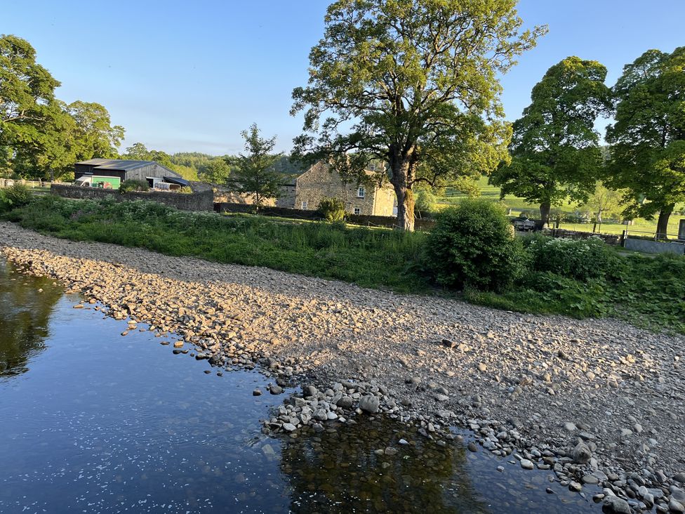 A river with a rocky shore and trees near a building at Bracken Cottage in Stanhope