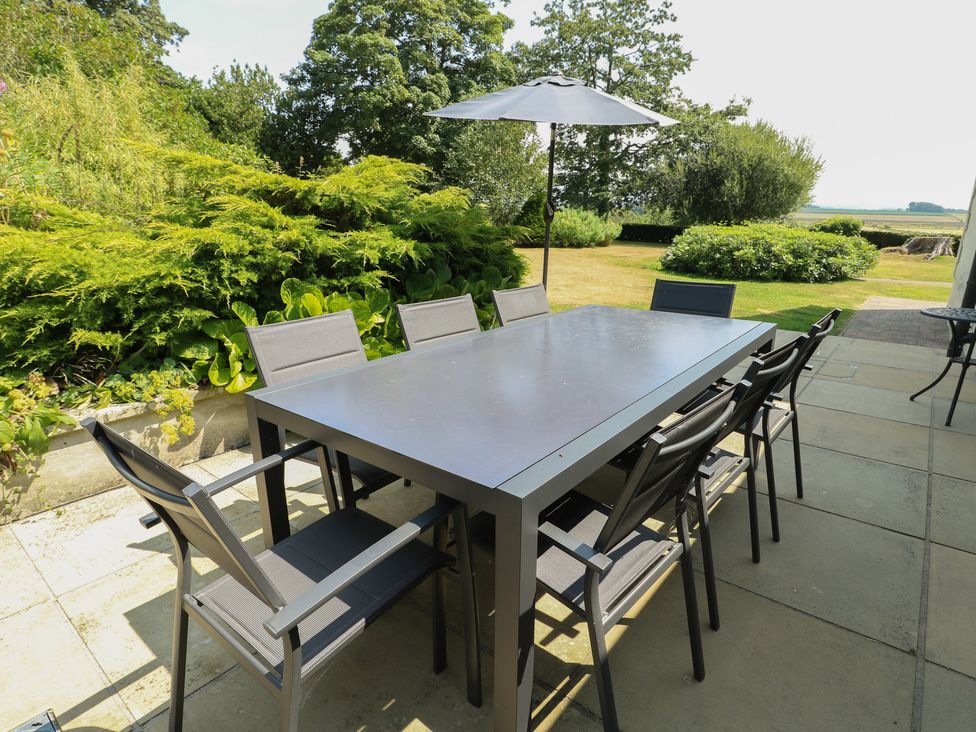 A garden with a table and chairs under an umbrella at Clynnog House in Dwyran near Newborough