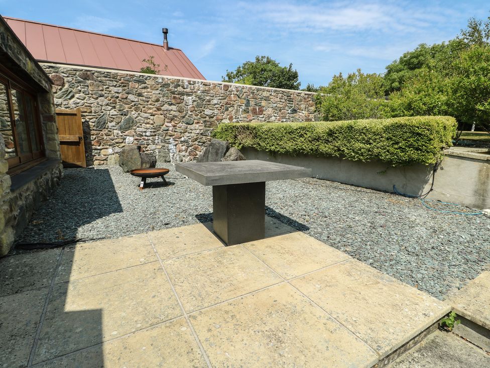 An outdoor area with a stone wall and a table at Clynnog House in Dwyran near Newborough