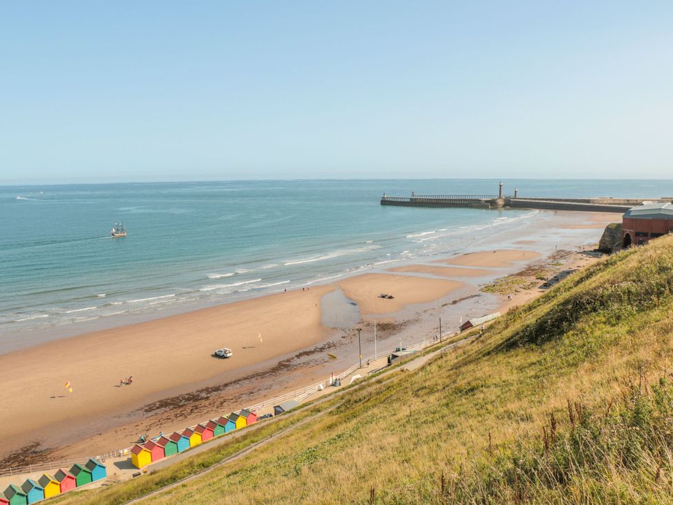 A beach with colorful huts and a pier at Sail Away, 17 Union Mill in Whitby