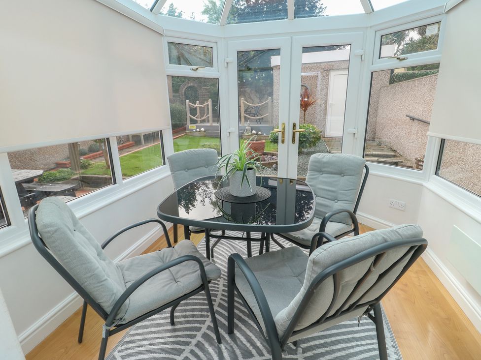 A conservatory with a glass table and four chairs at Glasfryn in Holyhead