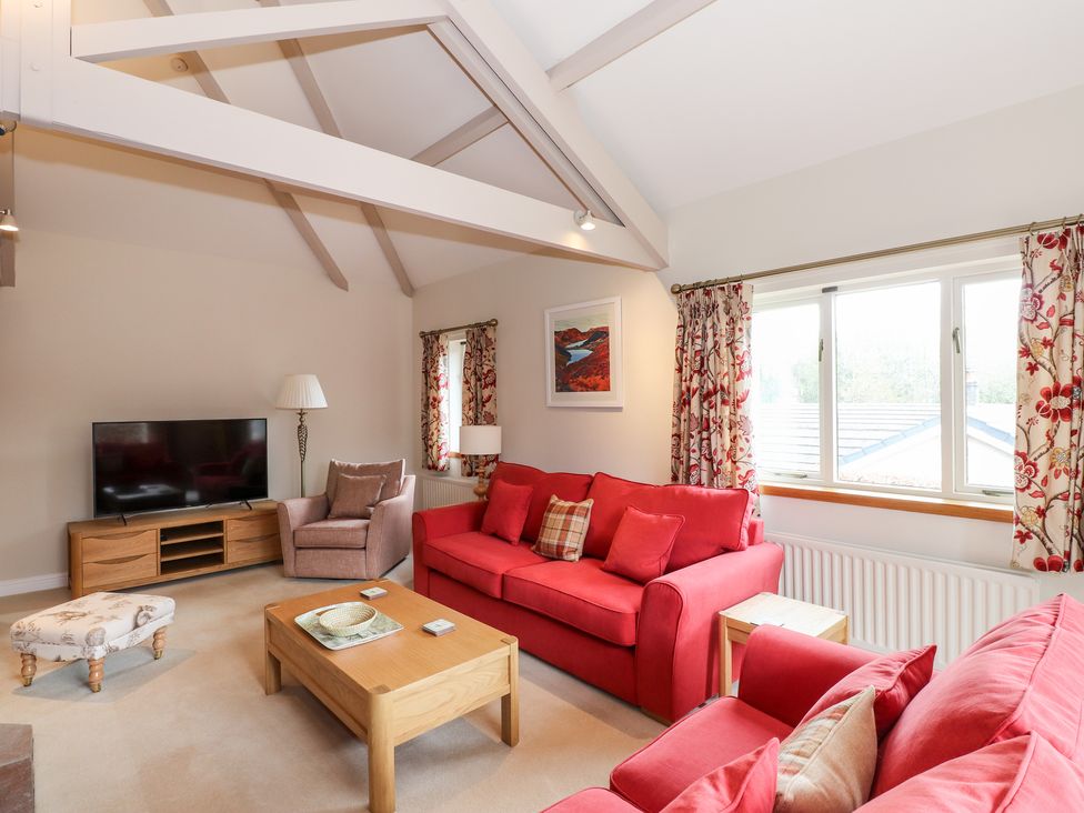 A living room with red sofas a beige armchair wooden coffee table and a TV on a wooden stand at Edencroft in Greystoke