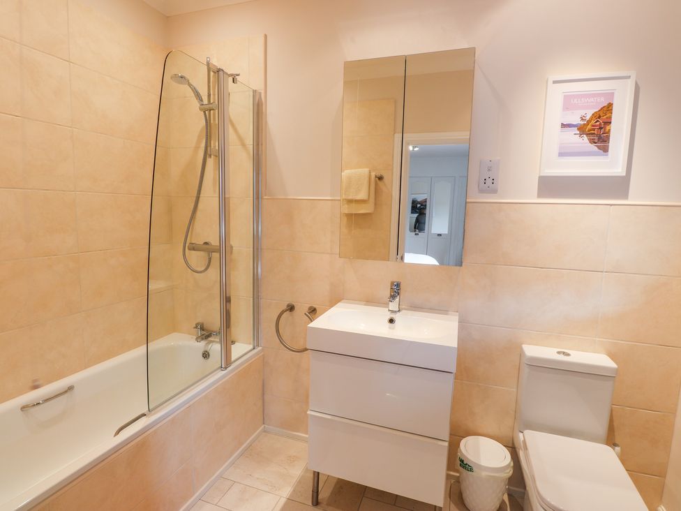 A bathroom with a bathtub and shower beside a sink with a mirror and a toilet at Edencroft in Greystoke
