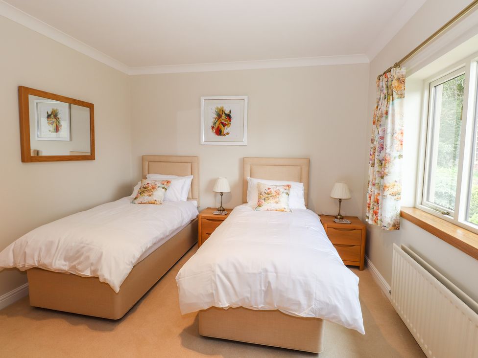 A bedroom with two single beds white bedding floral pillows wooden bedside tables and a window with floral curtains at Edencroft in Greystoke