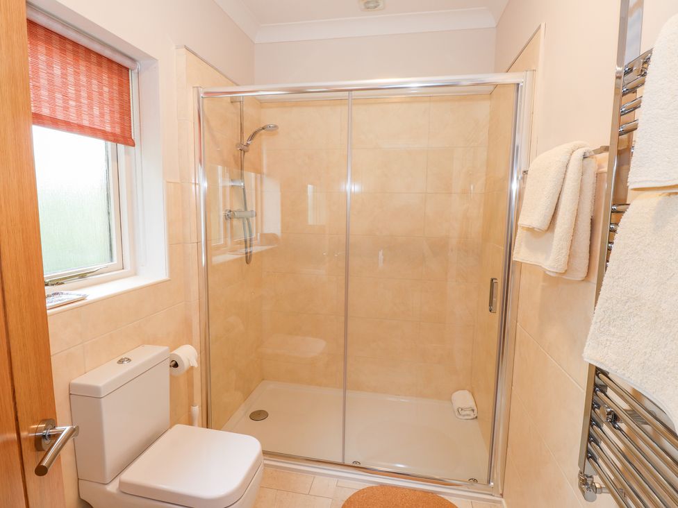 A bathroom with a shower enclosure a toilet a window with an orange blind and towels on a radiator at Edencroft in Greystoke