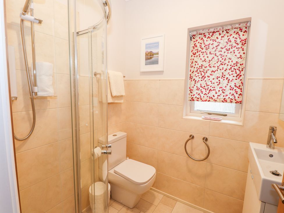A bathroom with a shower cubicle toilet sink and a window with a floral patterned blind at Edencroft in Greystoke