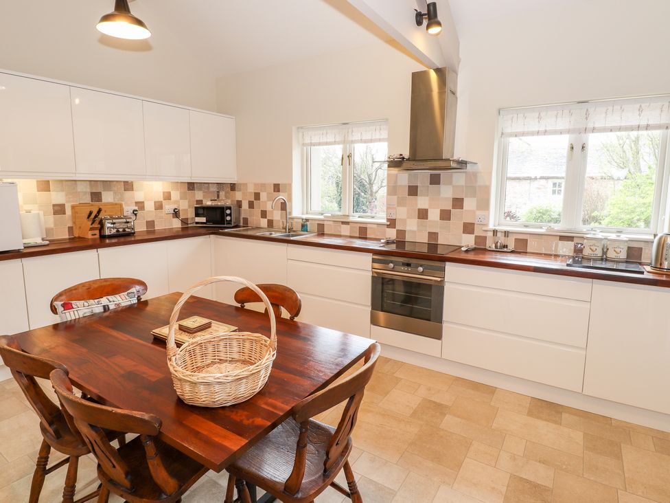 A kitchen with wooden table and chairs white cabinets and tiled backsplash at Edencroft in Greystoke