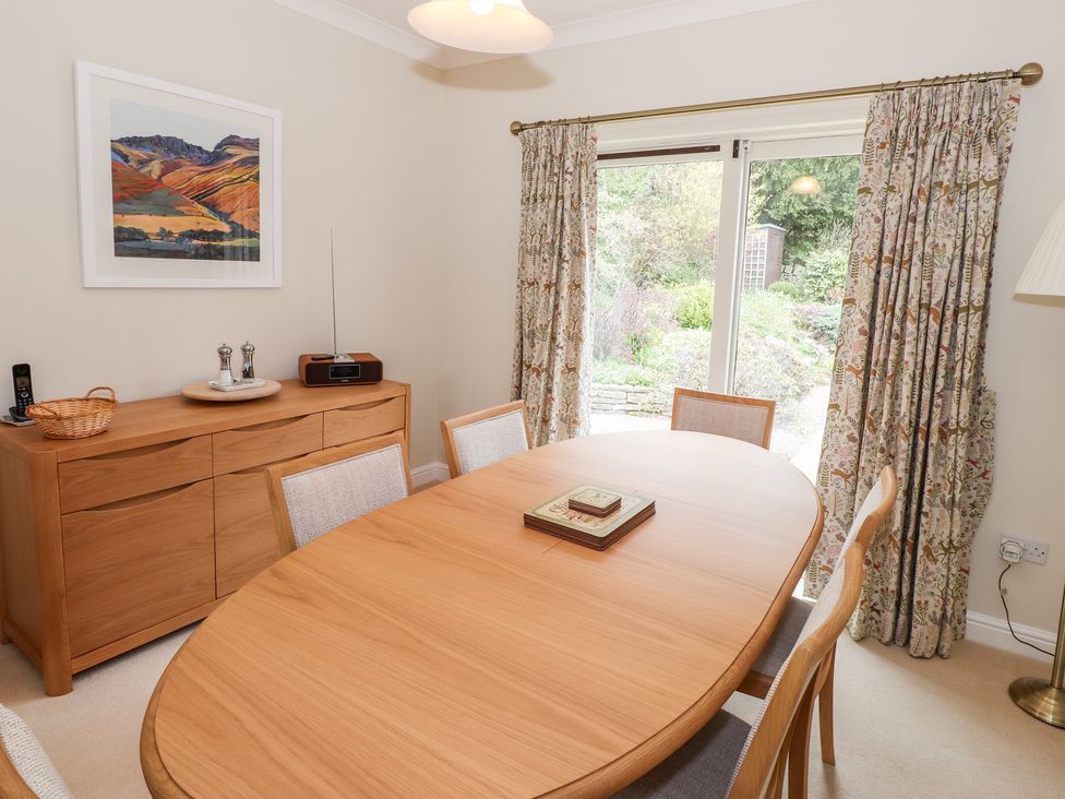 A dining room with a wooden table and chairs wooden sideboard with a radio and condiments sliding glass doors with patterned curtains at Edencroft in Greystoke