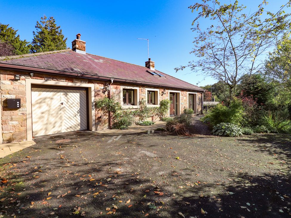 A stone house with a garage door and windows surrounded by trees and shrubs at Edencroft in Greystoke