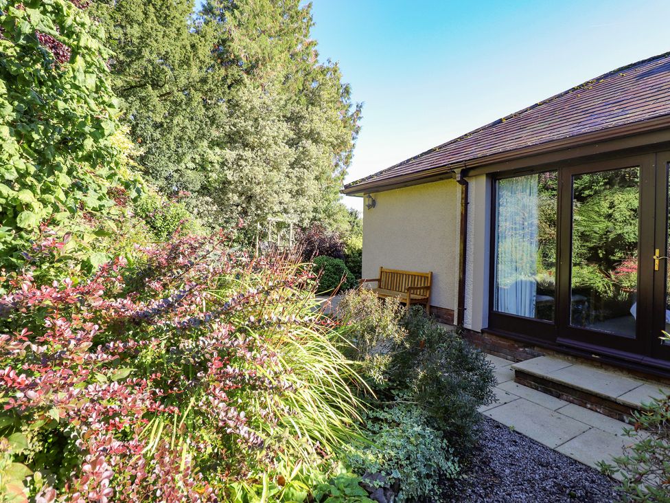A garden with shrubs and a bench next to a house with large glass doors at Edencroft in Greystoke