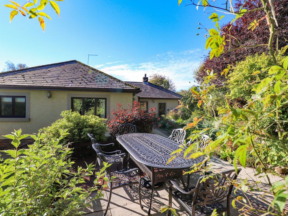 An outdoor patio area with a metal table and chairs surrounded by plants and a single-story house in the background at Edencroft in Greystoke