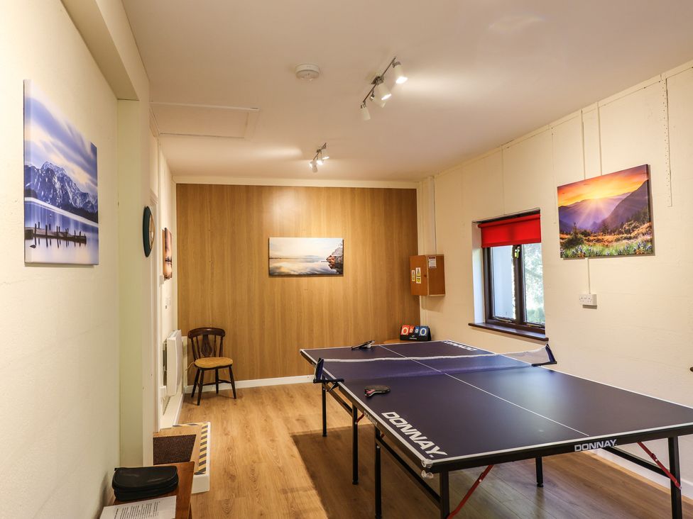 A recreation room with a ping pong table, wooden chair, framed landscape photos and a window with a red blind at Edencroft in Greystoke