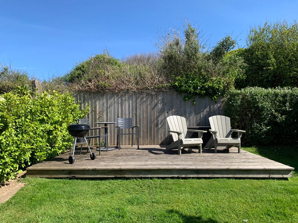 A garden with a deck, a grill, and two chairs at Lavender Barn Crantock