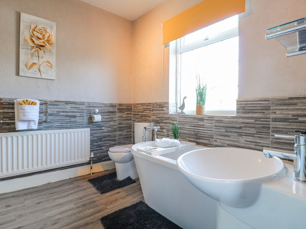A bathroom with a bathtub, toilet, sink, and window at Ley Fields Farm in Cheadle