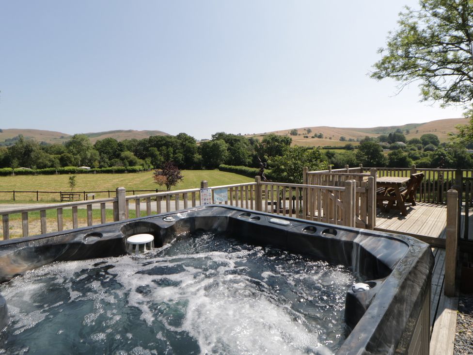 A hot tub on a wooden deck with a view of fields and hills at Hares Rest in Nantmel near Rhayader