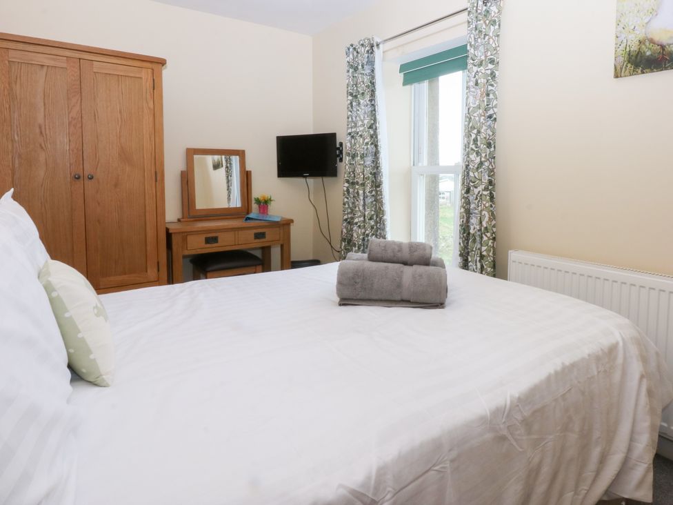 A bedroom with a bed, wardrobe, television, and mirror at Tregynrig Bach in Cemaes Bay