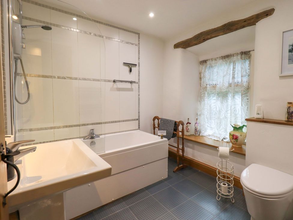 A bathroom with a bathtub and shower along with a toilet and sink at Fellside Cottage in Bowness-On-Windermere