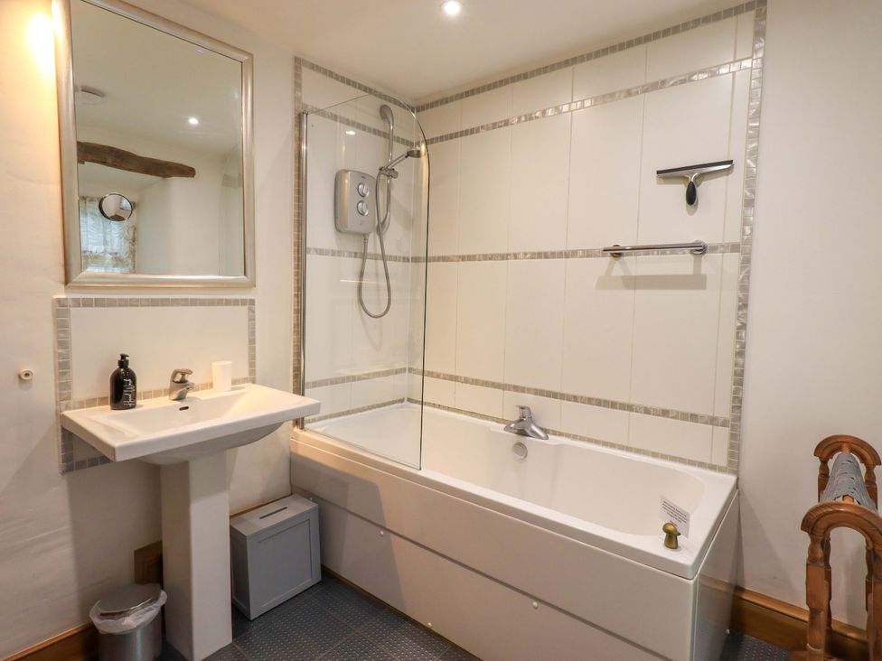 A bathroom with a bathtub, shower, sink and mirror at Fellside Cottage in Bowness-On-Windermere