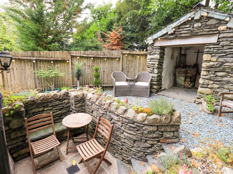 A garden with a stone wall, table, chairs, and a shed at Fellside Cottage in Bowness-On-Windermere