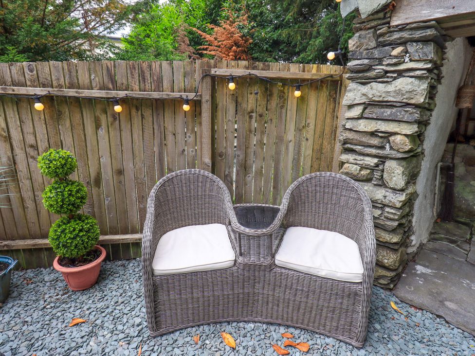 A garden with a wicker bench and a topiary planter at Fellside Cottage in Bowness-On-Windermere