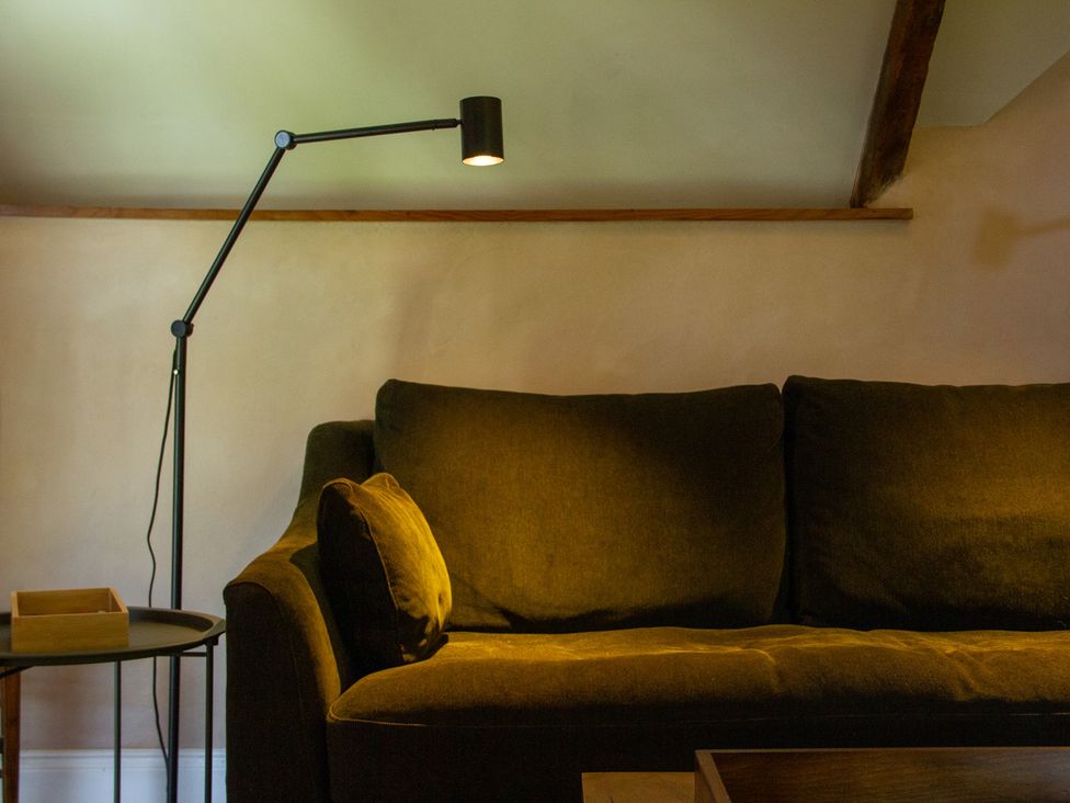 A living room with a sofa and floor lamp at Carrows Stable in Morwenstow