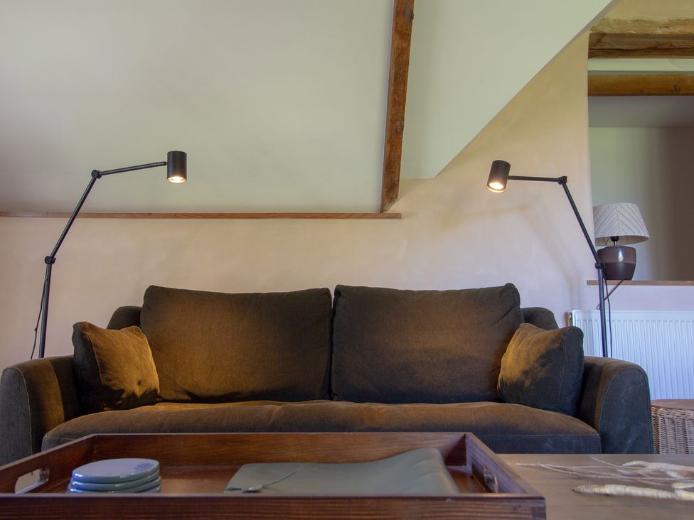 A living room with a sofa and floor lamp at Carrows Stable in Morwenstow