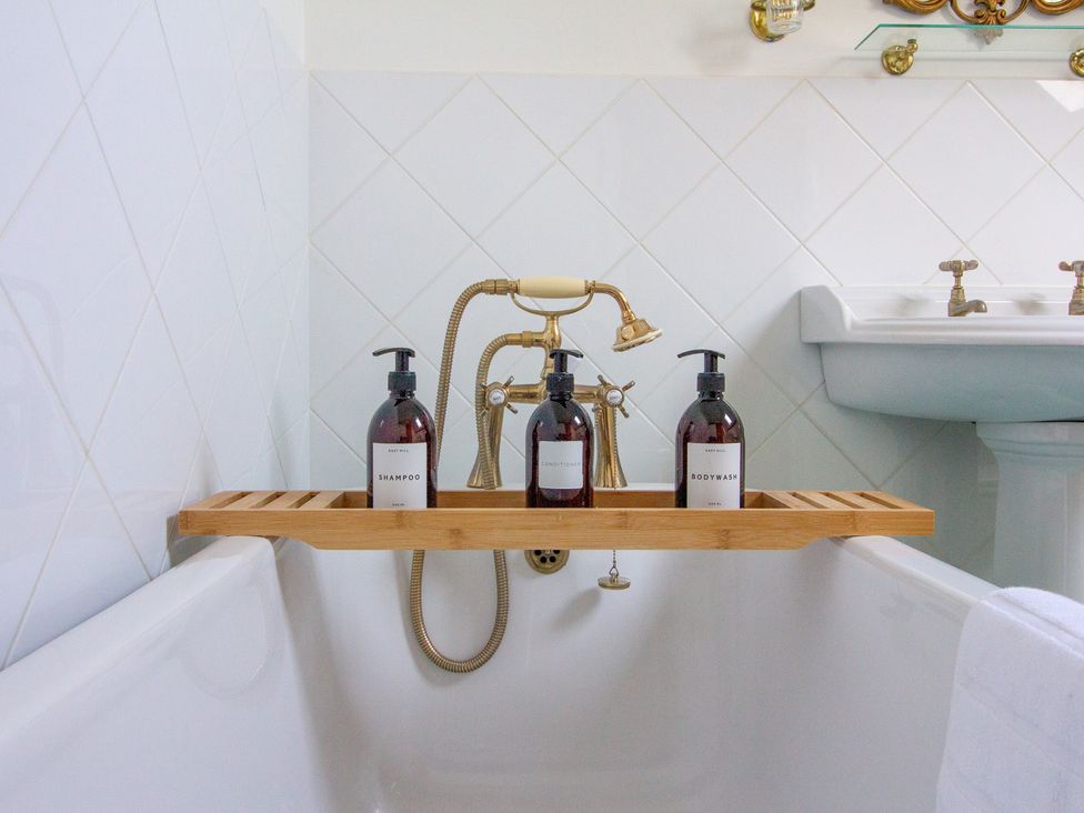 A bathtub with shampoo and body wash bottles in a bathroom at Carrows Stable in Morwenstow