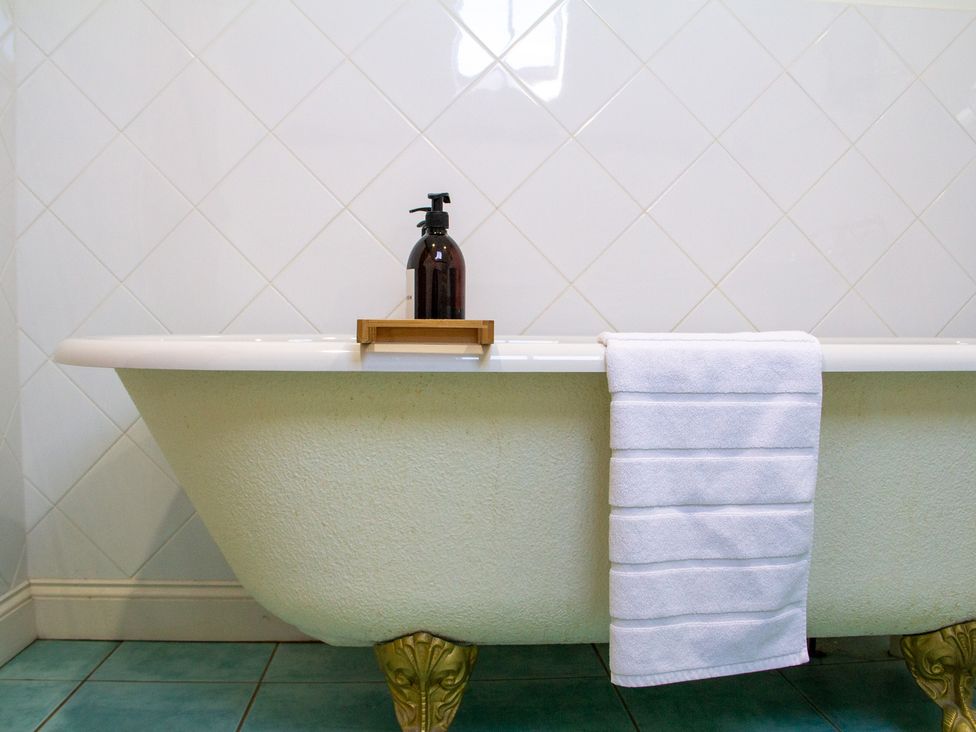 A bathtub with a bottle on a shelf and a towel at Carrows Stable in Morwenstow