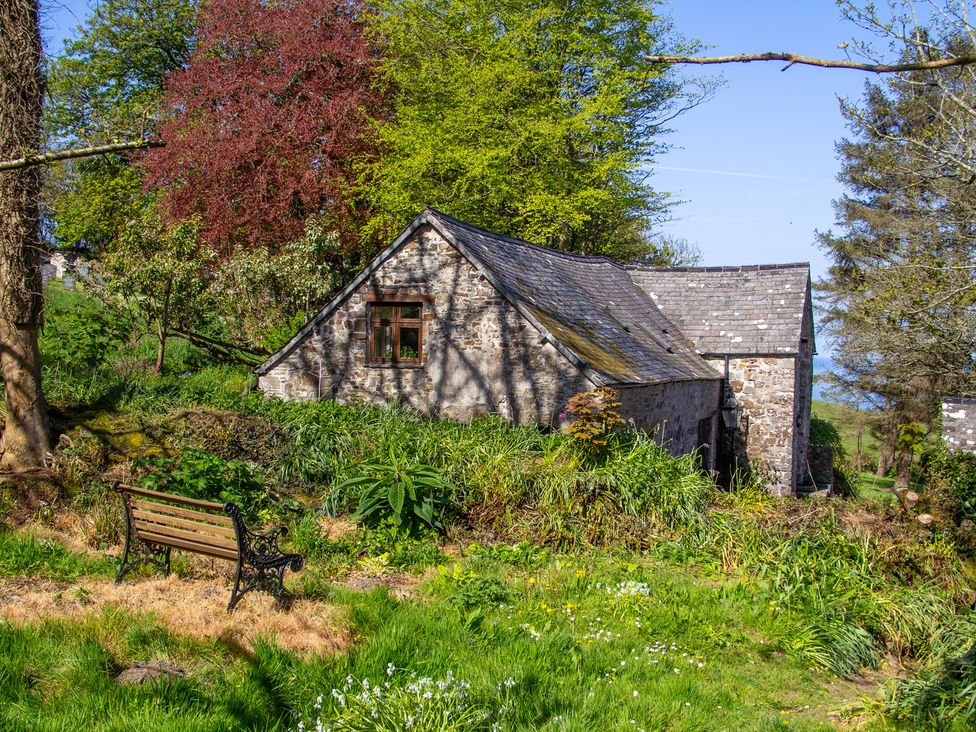 A building surrounded by trees and a bench at Carrows Stable Morwenstow