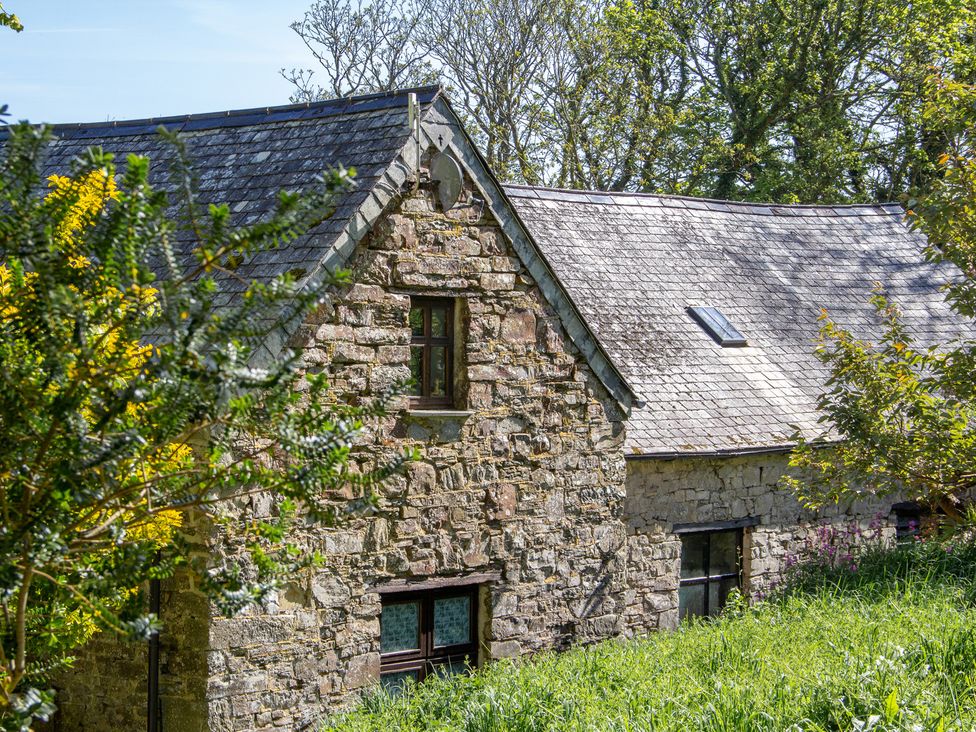 A stone building with a sloped roof and windows at Carrows Stable in Morwenstow