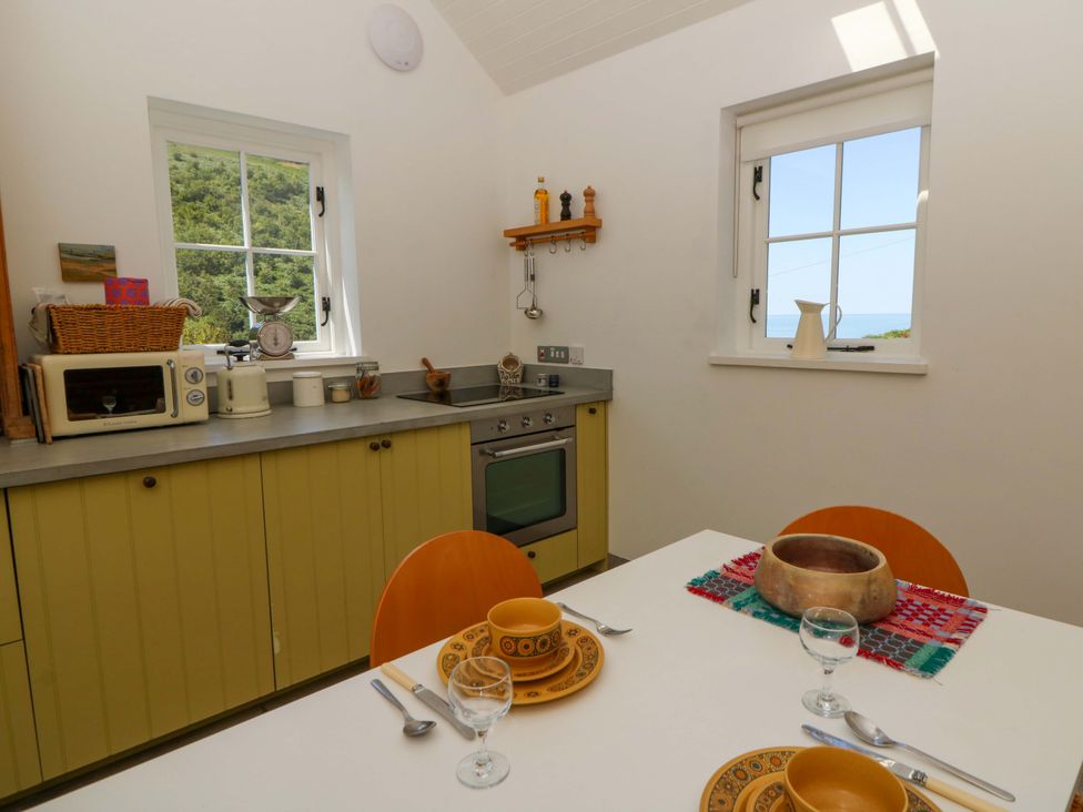 A kitchen with cabinet and dining table at Dolwylan Barn Cwmtydu near New Quay