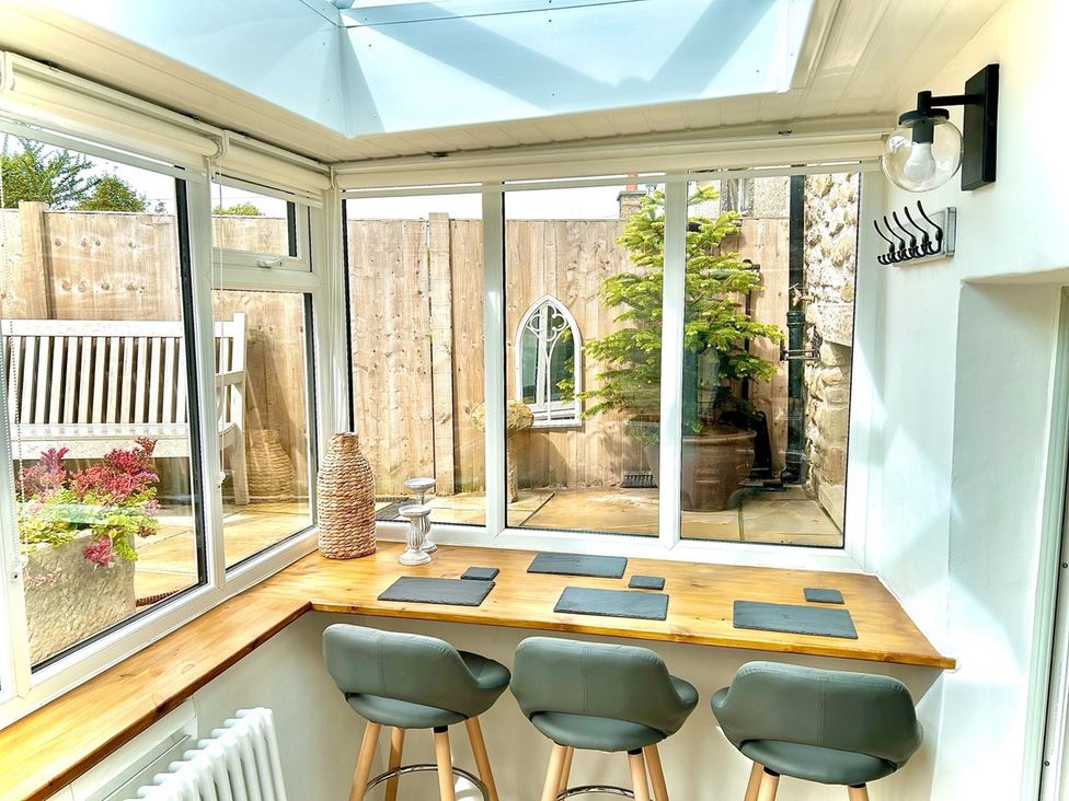 A conservatory with a table and bar stools at Lydgate Cottage in Eyam