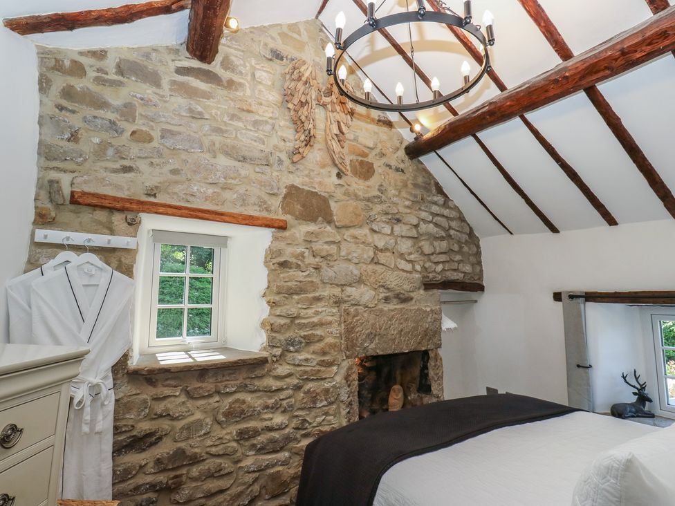 A bedroom with a stone wall and a chandelier at Lydgate Cottage in Eyam