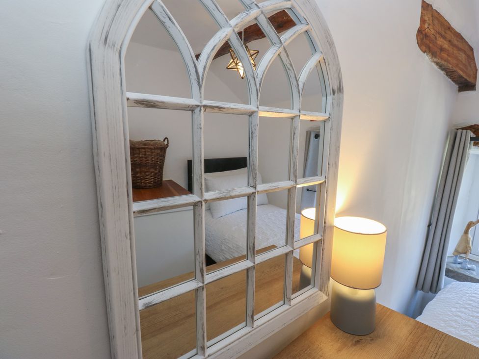 A mirror reflecting a bedroom with a lamp and basket at Lydgate Cottage in Eyam