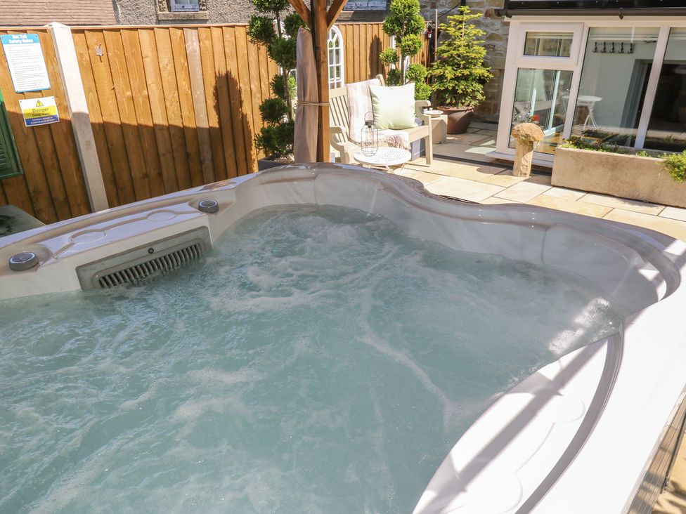 A hot tub with water in a garden with a chair and plants at Lydgate Cottage in Eyam