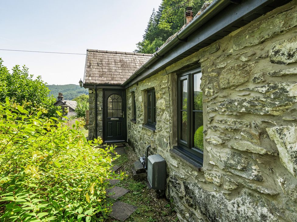 An exterior view of a cottage with stone walls and a pathway at Tyn Y Ffynnon in Betws-Y-Coed