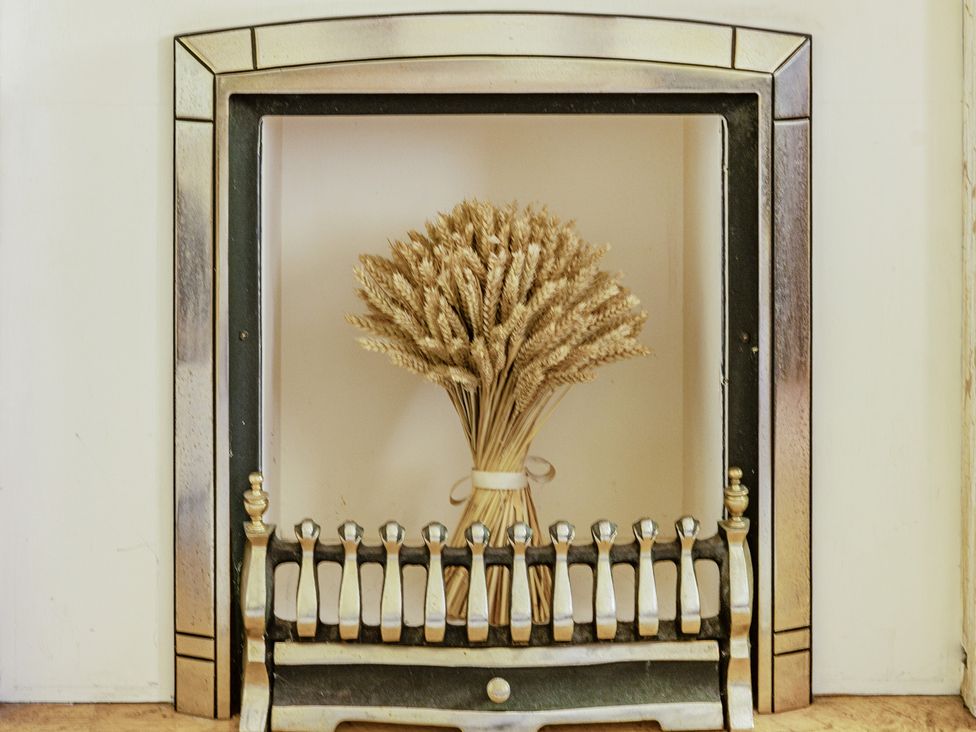 A fireplace with a wheat bouquet and fireplace fender at Tyn Y Ffynnon in Betws-Y-Coed